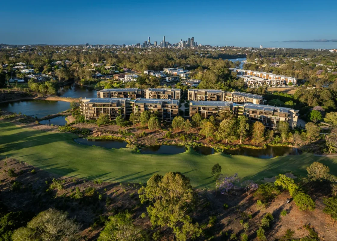 Aerial view of an award-winning Somerset apartment complex surrounded by trees and green spaces, with a city skyline visible in the background under a clear blue sky.